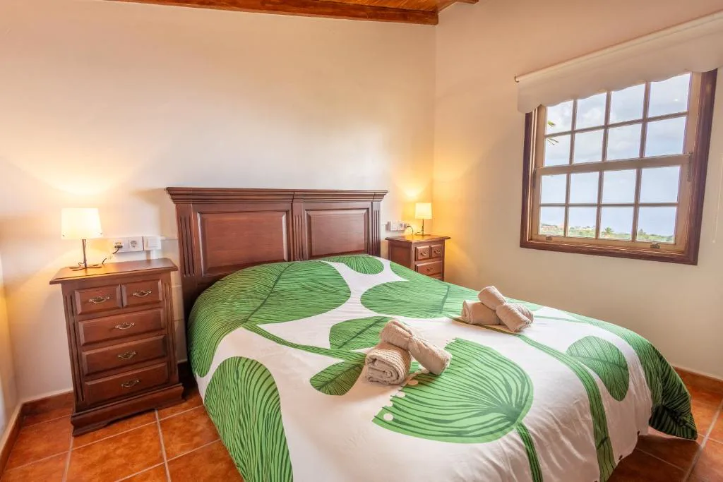 Dormitorio con cabecero de madera tallada y colcha verde de hojas, Casa de Los Establos