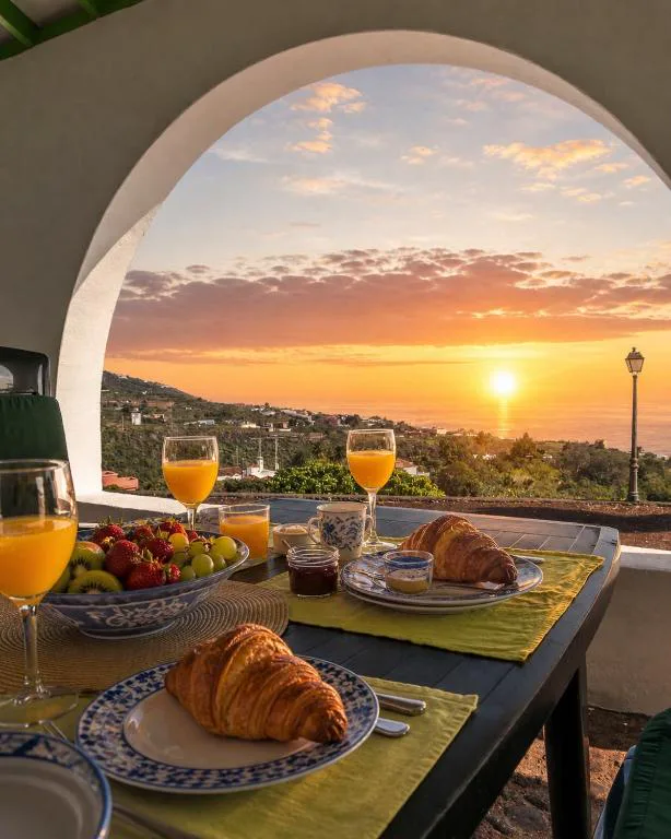 Desayuno con fruta fresca y croissants bajo un arco con vistas al amanecer sobre el mar, Casa de Los Establos
