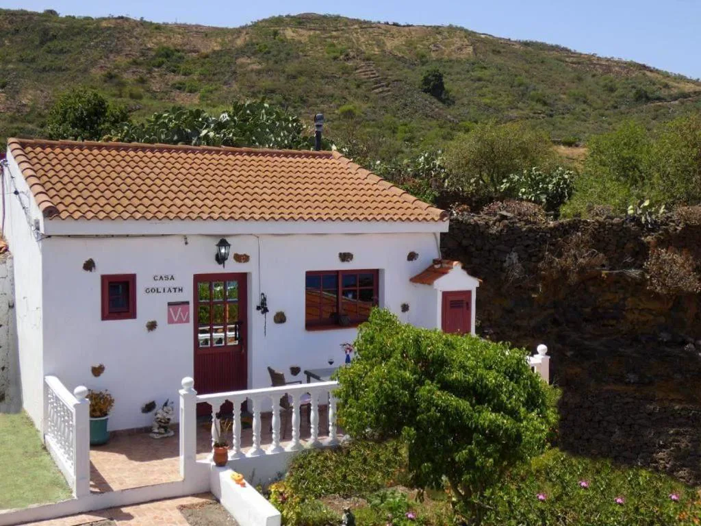 Fachada blanca con tejado de teja y montañas al fondo, Casa Goliath, en Isora, El Hierro