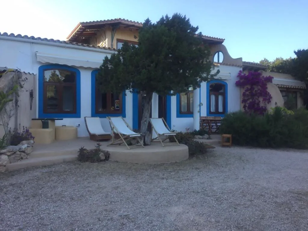 Fachada blanca y azul con hamacas de madera bajo un árbol y buganvillas, Casa Goro