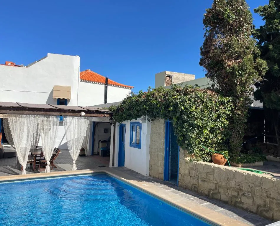 Fachada blanca y azul con piscina y cortinas de gasa en el porche, Casa Juan Vera, en Charco del Pino, Granadilla de Abona, Tenerife