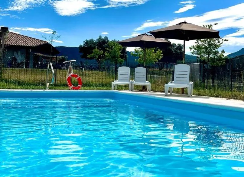 Piscina azul con sombrilla y tumbonas rodeada de césped