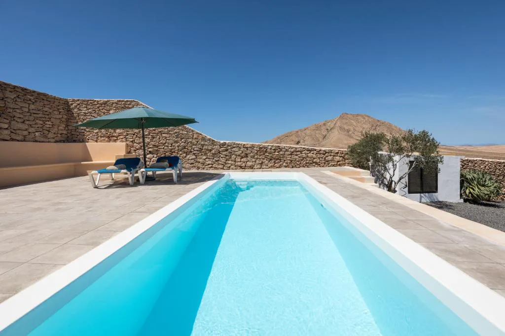 Piscina alargada entre muros de piedra volcánica con la montaña de Tindaya al fondo, Casa Marisa
