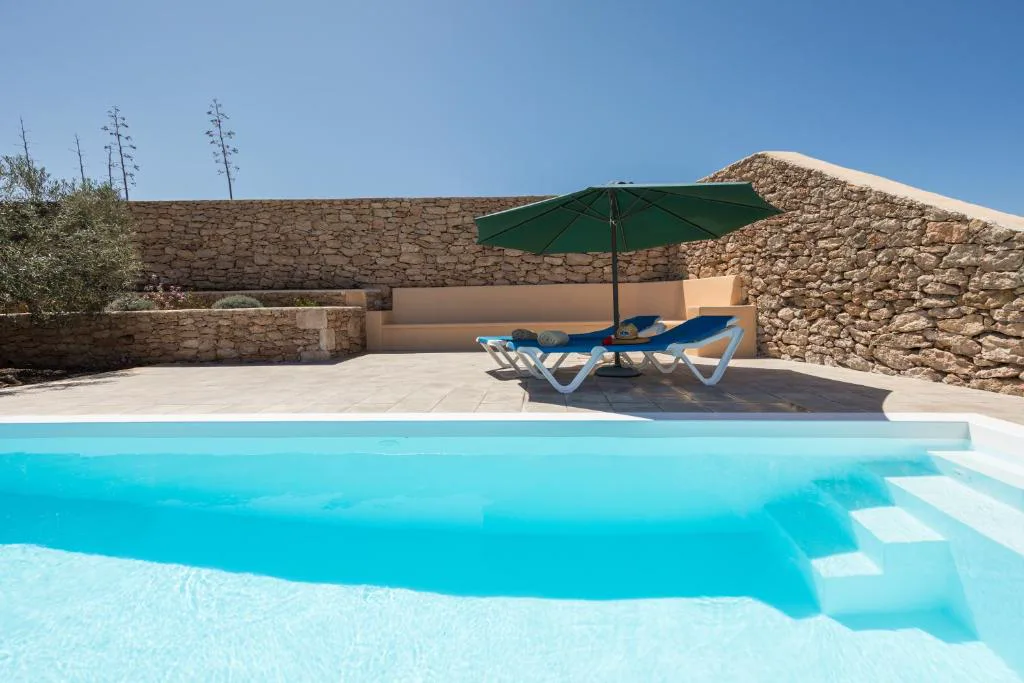 Piscina climatizada con sombrilla verde y tumbonas junto al muro de piedra, Casa Marisa