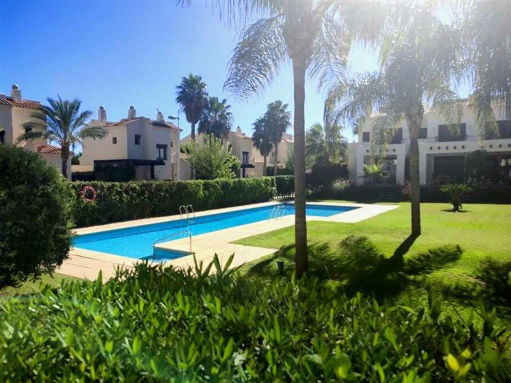 Piscina comunitaria entre palmeras y césped del resort