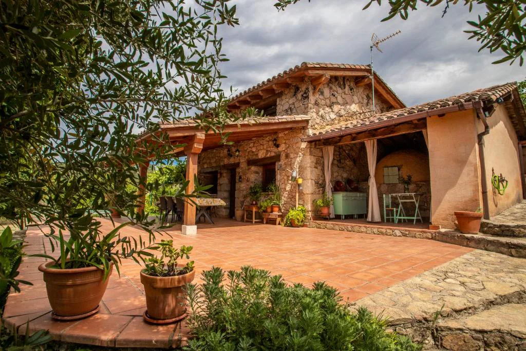 Casa de piedra con porche de teja y jardín con macetas
