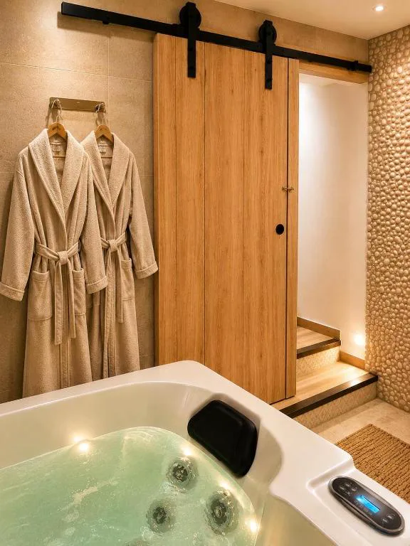 Bañera de hidromasaje con albornoz colgado junto a una puerta de madera