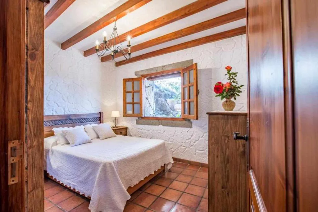 Dormitorio con paredes de piedra vista y techo de vigas de madera, Casa Oronado
