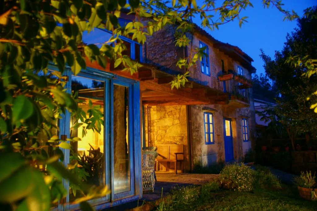 Fachada de piedra iluminada al anochecer con ventanas y balcón en azul, Casa Perfeuto Maria