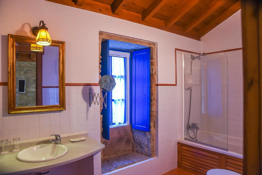 Baño tradicional con espejo dorado y ventana de piedra en azul, Casa Perfeuto Maria