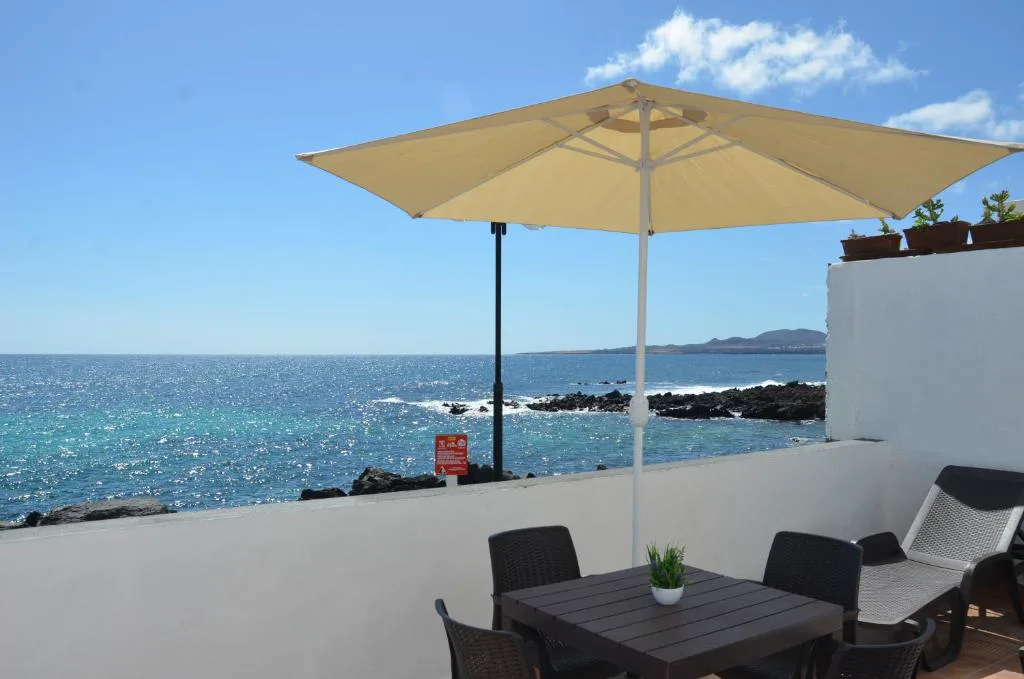 Terraza frente al mar con sombrilla y vistas a la costa volcánica de Punta Mujeres, Casa de la playa, Lanzarote