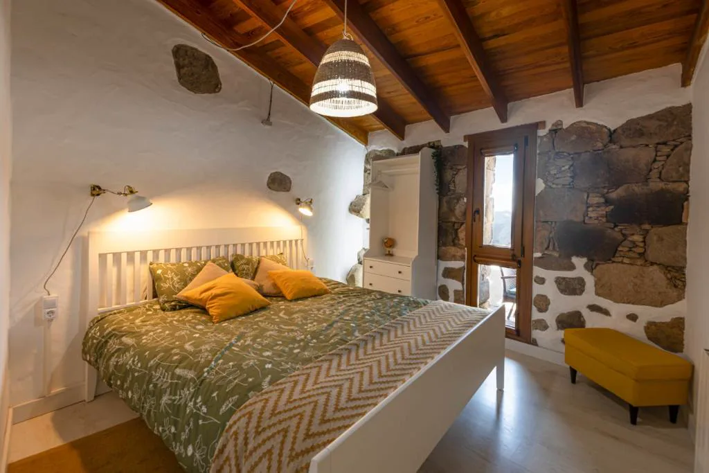 Dormitorio de piedra vista con cabecero blanco y ropa de cama verde estampada, Casa Rural Bentayga