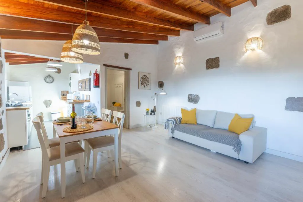 Salón con techos de madera vista, paredes blancas y sofá con cojines amarillos, Casa Rural Bentayga