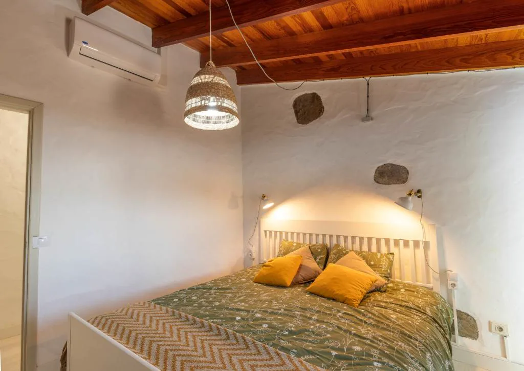 Dormitorio con pared de piedra vista y cojines amarillos sobre colcha verde, Casa Rural Bentayga
