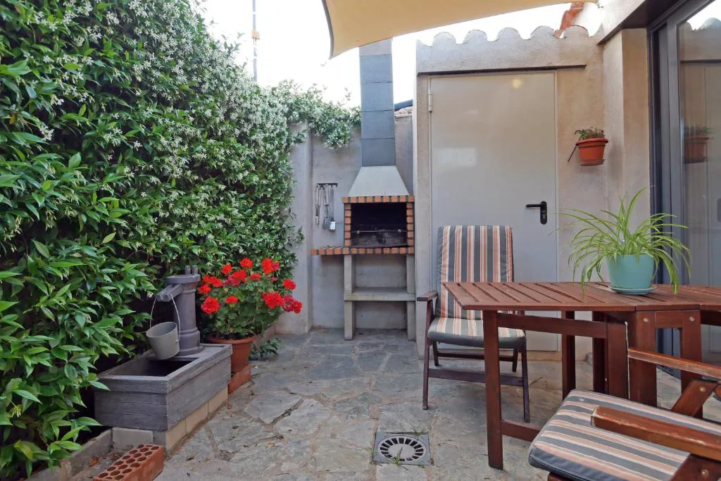 Patio con barbacoa, mesa de madera y hiedra