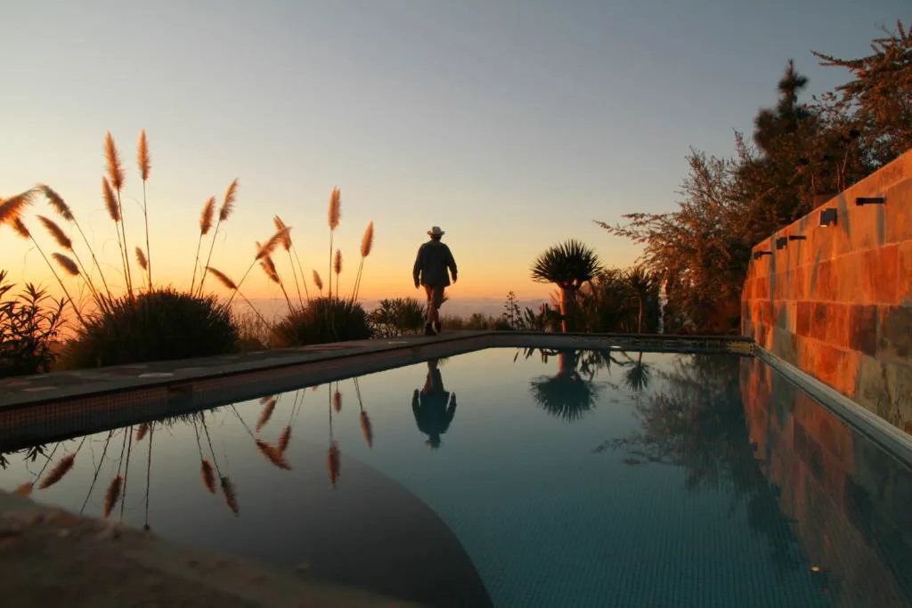 Piscina al atardecer con reflejo de plumeros y vistas al mar de nubes, Casa Rural El Refugio