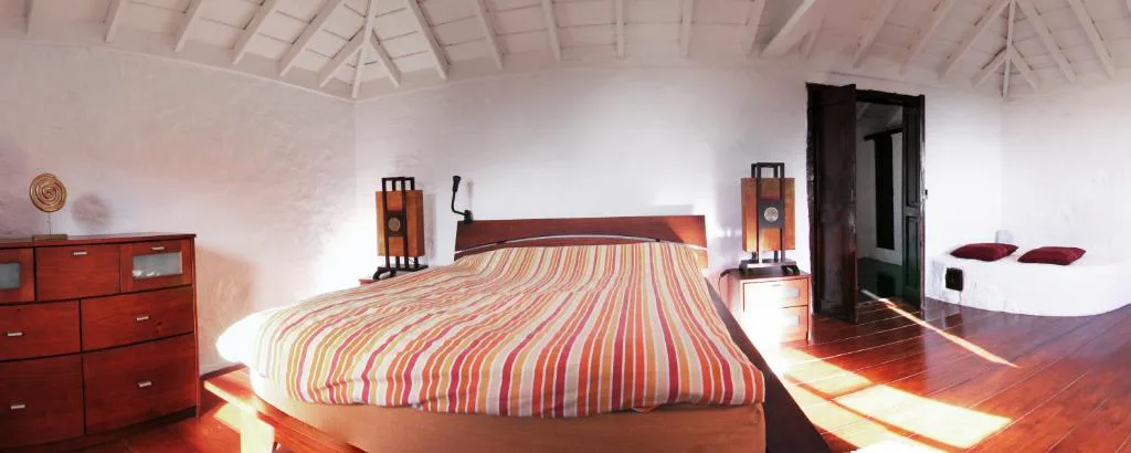 Dormitorio con cabecero de madera y colcha de rayas bajo techo abuhardillado, Casa Rural El Refugio