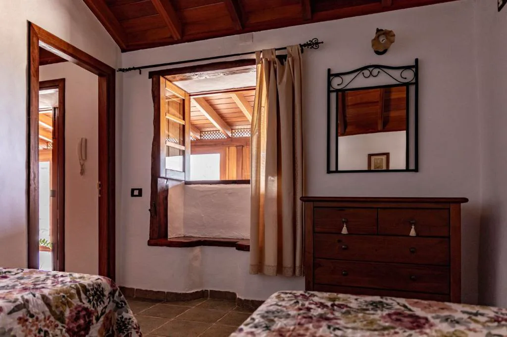 Dormitorio con ventana de madera abierta y cómoda antigua junto a un espejo de forja, Casa Rural La Palizada