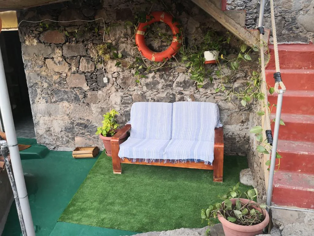 Rincón exterior con sofá de rayas azules junto a un muro de piedra con un salvavidas decorativo, Casa rural Los Órganos de Arguamul