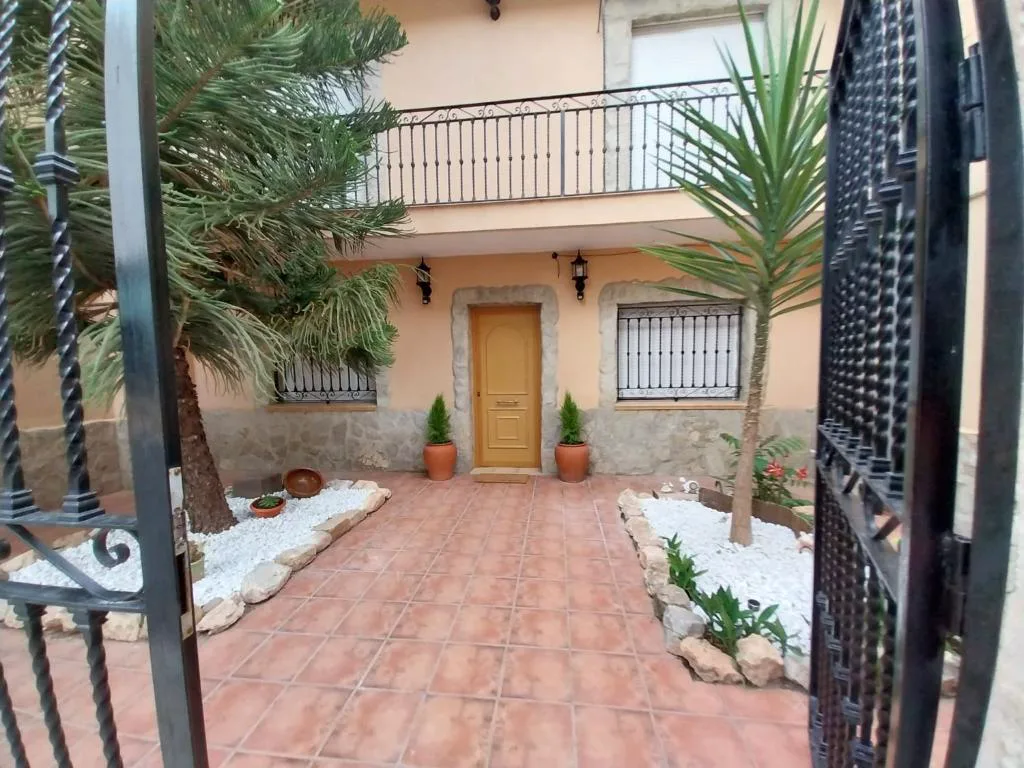 Fachada con patio de baldosas y palmeras de la casa rural en Casinos