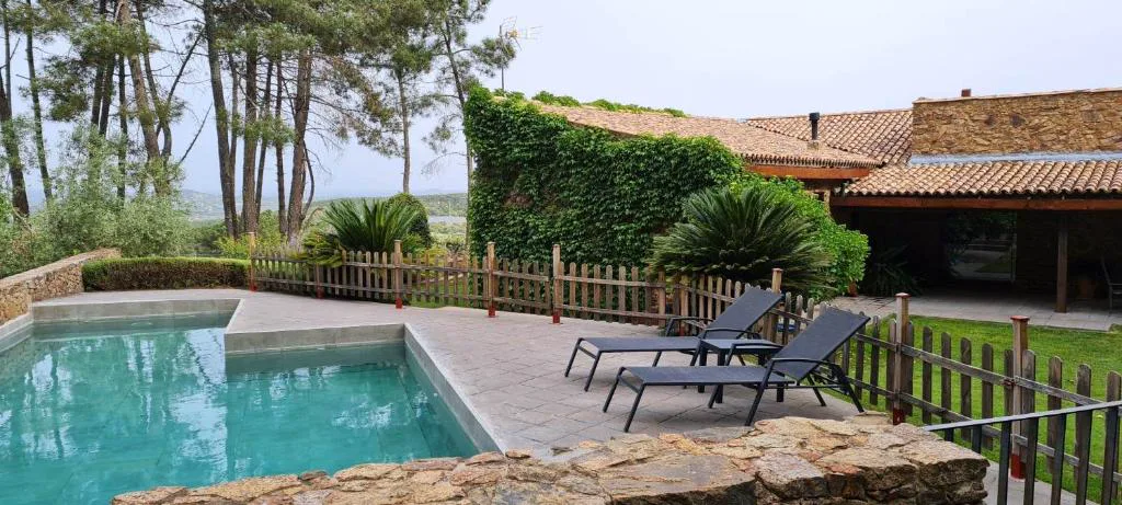 Piscina rodeada de pinos junto a la casa de piedra