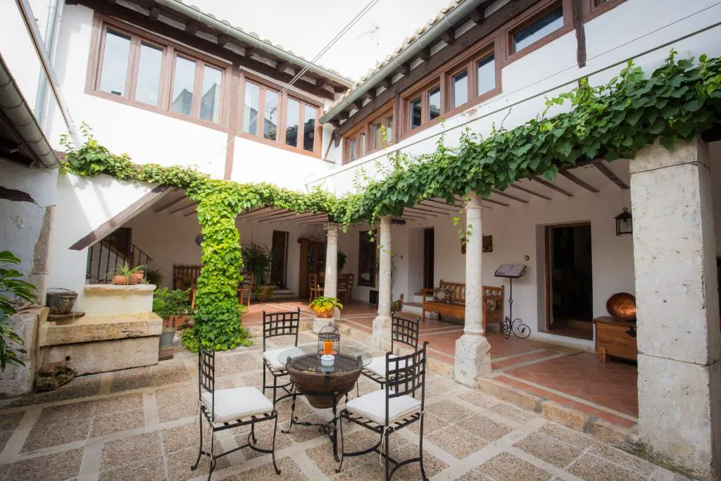 Patio interior de la casa rural con parras, columnas de piedra y mesas de forja