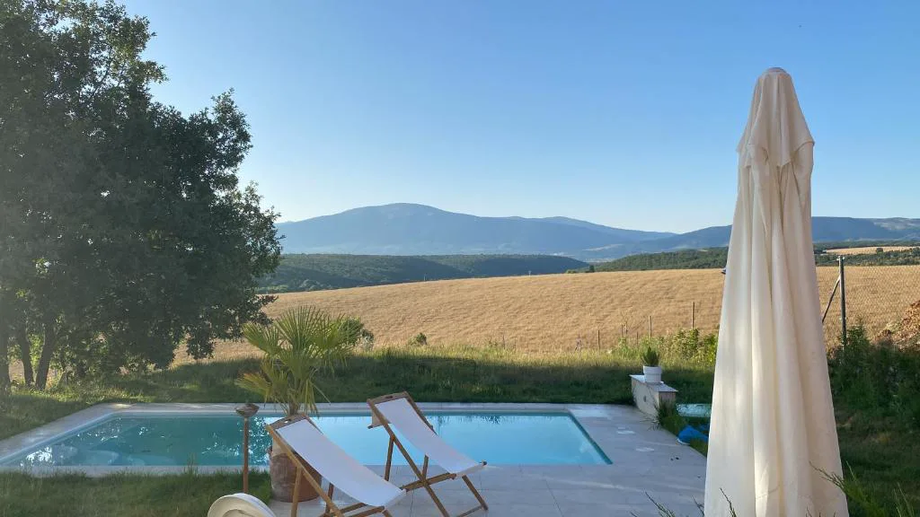 Piscina con sombrilla y campos dorados con la sierra al fondo