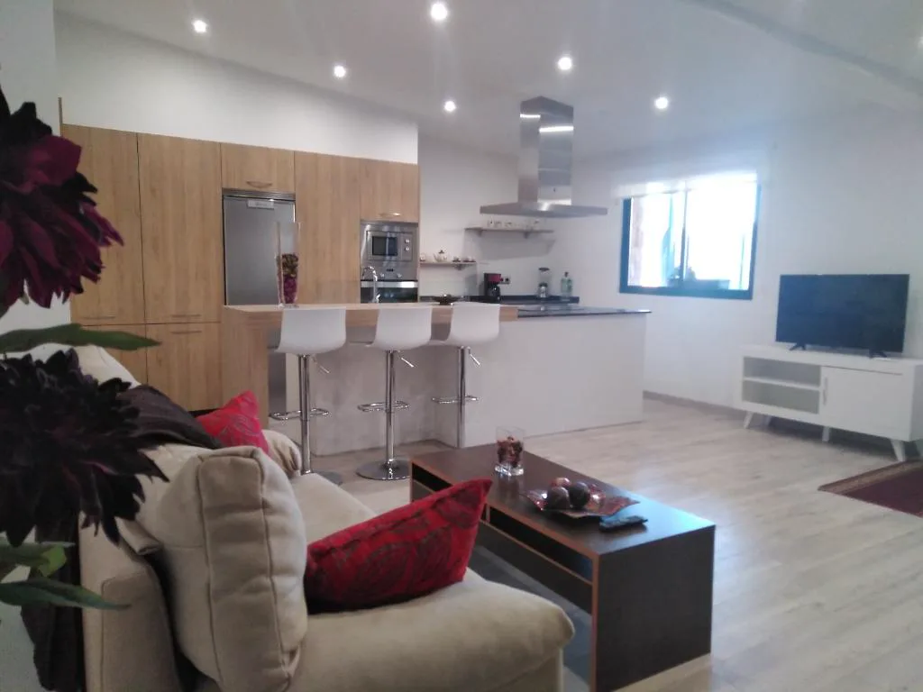 Salón y cocina abierta con sofá y flores rojas, Casa Spa en Montaña