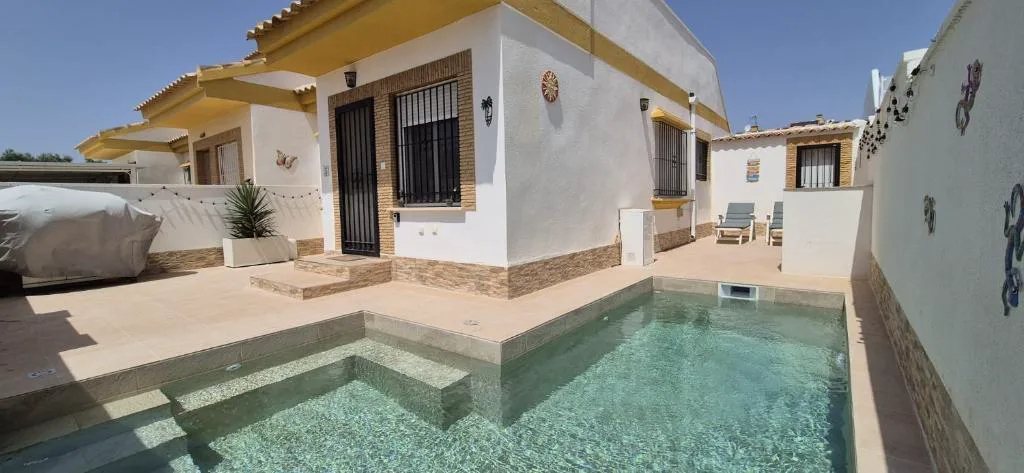 Piscina pequeña frente a una casa amarilla con patio