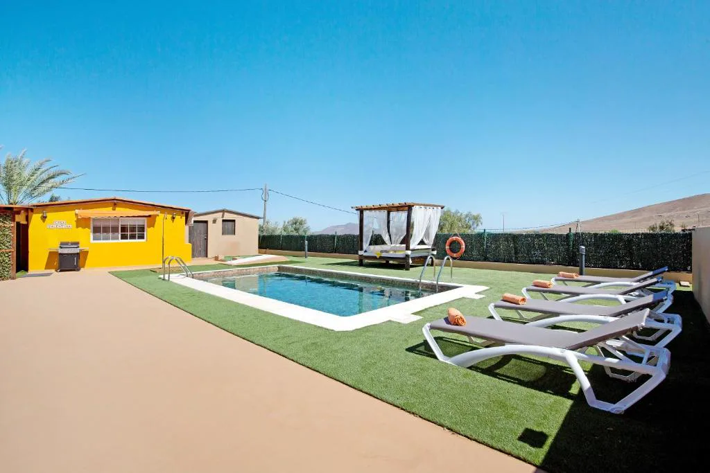 Piscina con tumbonas junto a la fachada amarilla de la casa, Casa Valentina