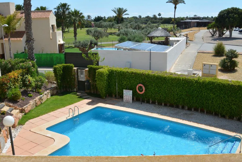 Piscina comunitaria con seto y palmeras junto a las casas del resort
