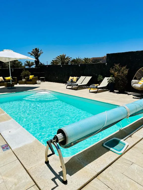 Piscina privada en un día soleado junto a tumbonas y sombrilla, Casa Volcanes