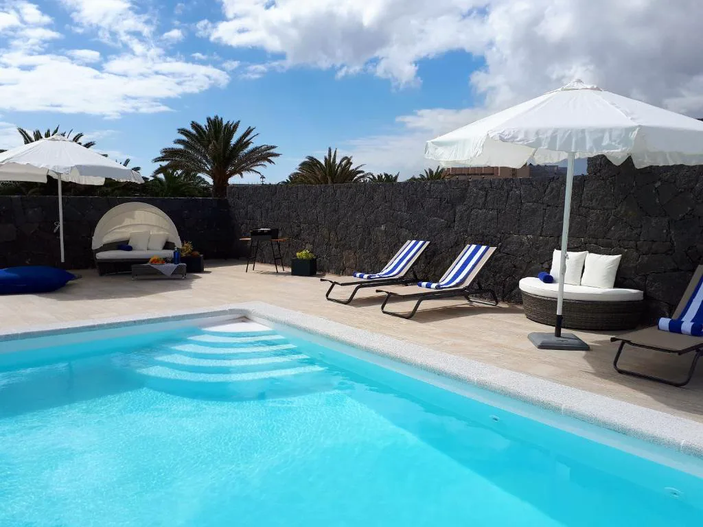 Piscina privada climatizada junto a un muro de piedra volcánica de Casa Volcanes, en Costa Teguise, Lanzarote