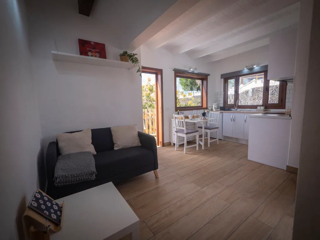 Salón con sofá azul marino y cocina abierta en tonos blancos, Casa volcánica El Cabezo