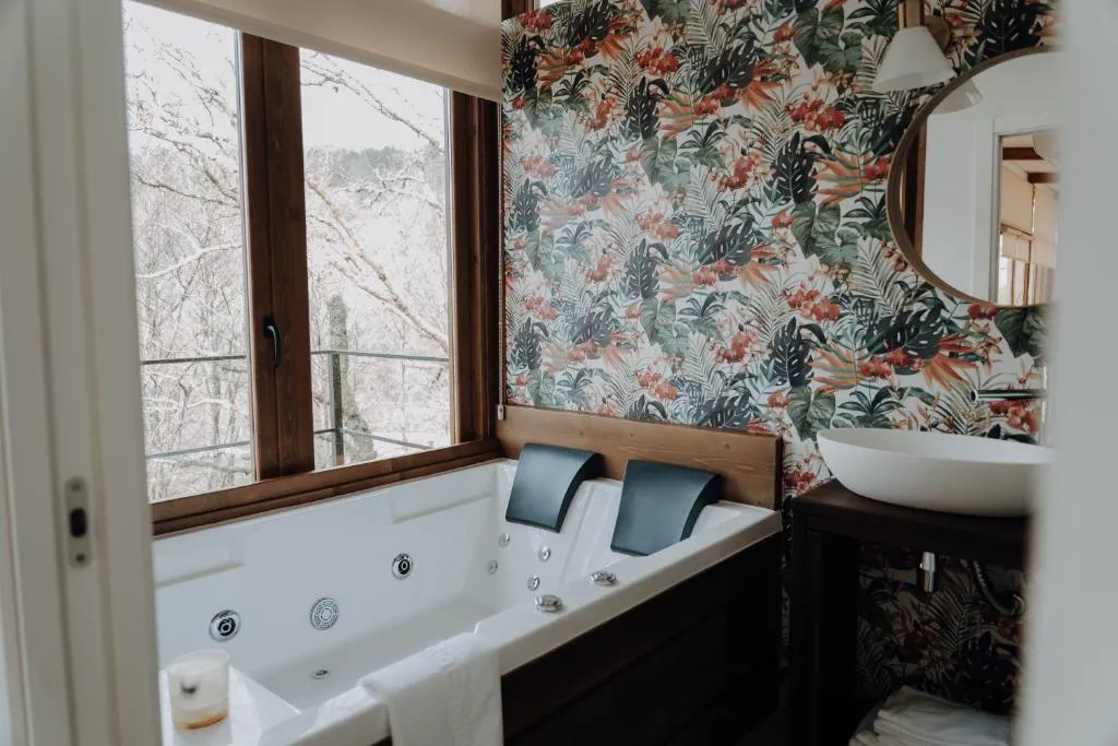 Bañera de hidromasaje junto a la ventana con vistas al bosque nevado, en una cabaña de Casal Oseira