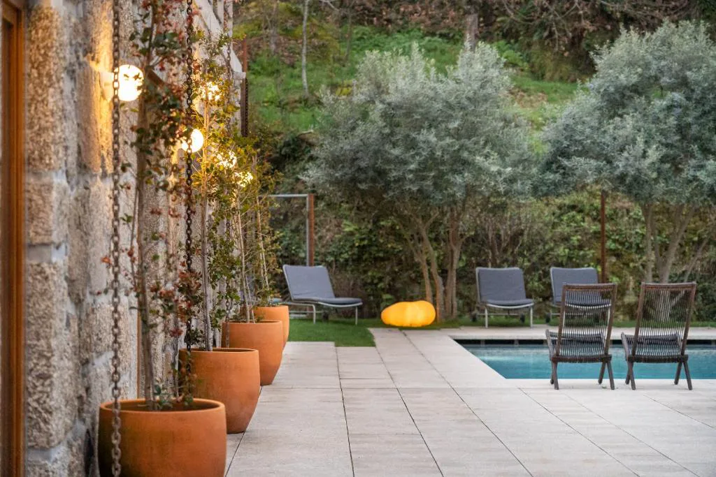 Terraza junto a la piscina al atardecer, entre macetas de barro y árboles, Casas da Lapa