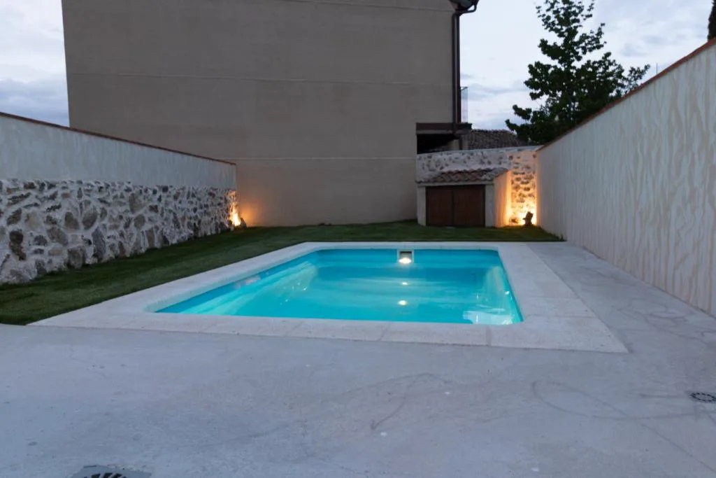 Piscina iluminada al anochecer junto a un muro de piedra