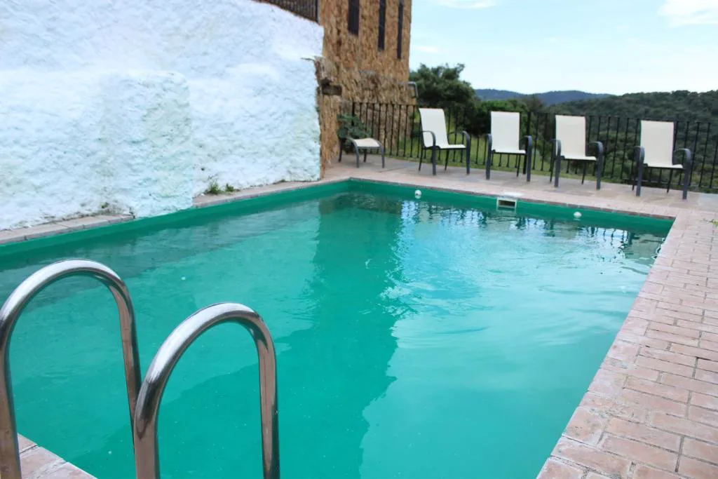 Piscina con escalera y sombrillas junto a una casa de piedra