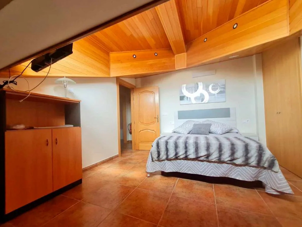 Dormitorio con techo de madera y cama con cabecero blanco