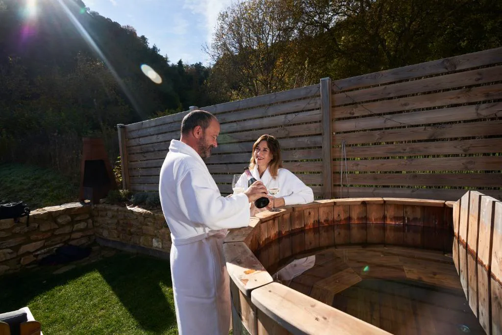 Pareja con albornoz junto a un jacuzzi de madera exterior