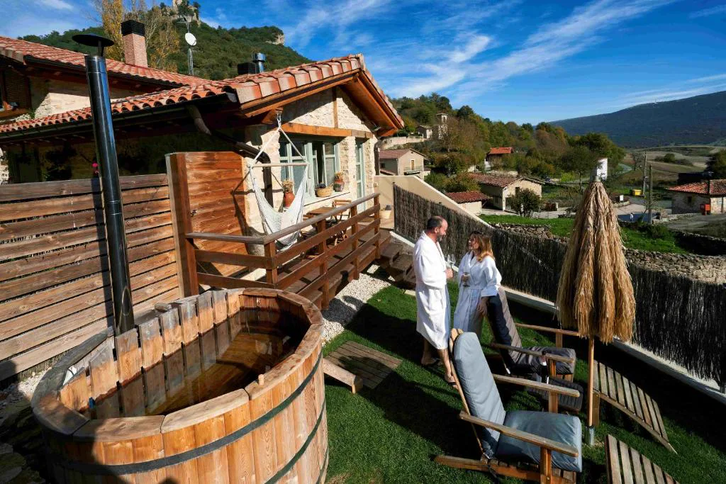 Terraza con jacuzzi de madera y sombrillas frente a la montaña