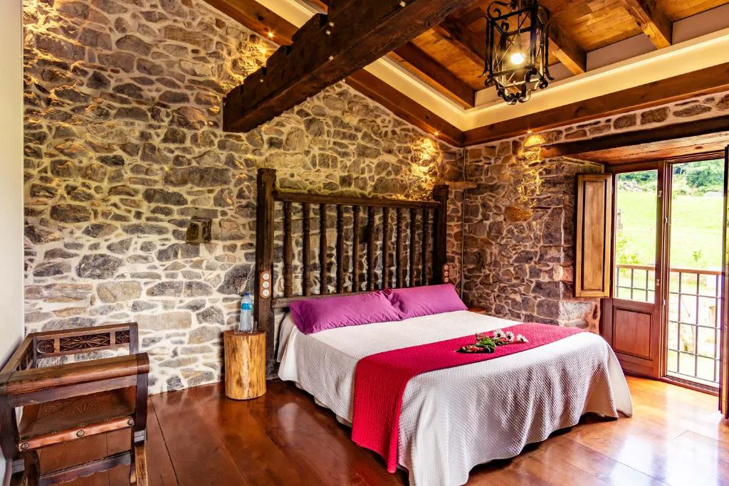 Habitación de piedra y vigas con cama de cabecero de madera y colcha rosa