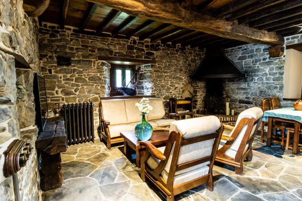 Salón de piedra con sofás y sillones de madera junto a un hogar