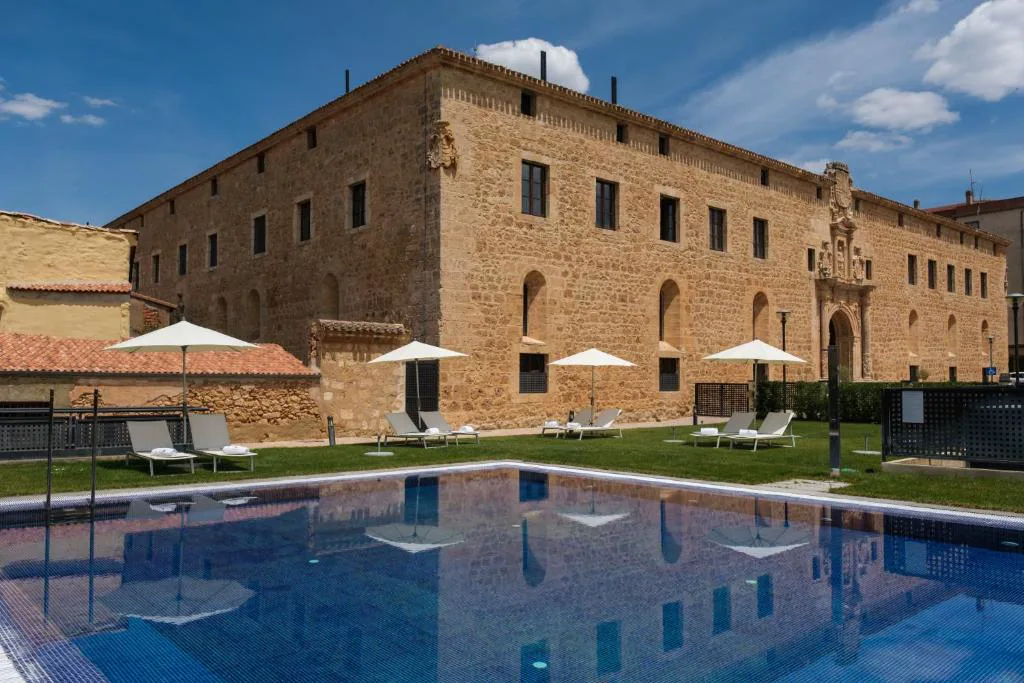 Fachada de piedra del antiguo edificio universitario con piscina exterior en Castilla Termal Burgo de Osma