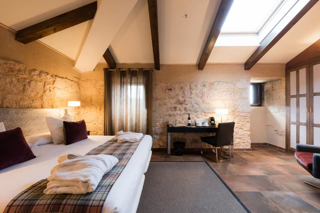 Habitación con vigas de madera vistas, muro de piedra y albornoces sobre la cama