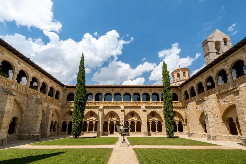 Claustro de arcos del monasterio con jardín central y cielo azul