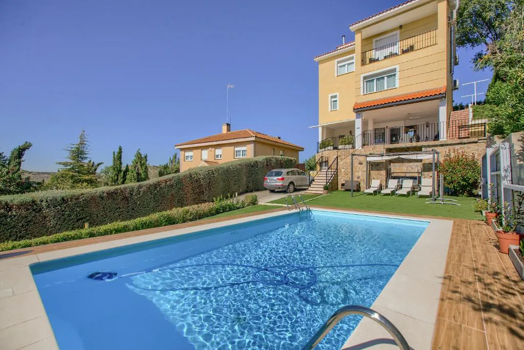 Piscina azul rodeada de césped frente a una casa de tres alturas