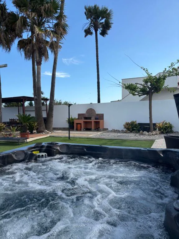 Jacuzzi exterior en un jardín con palmeras y una pérgola blanca