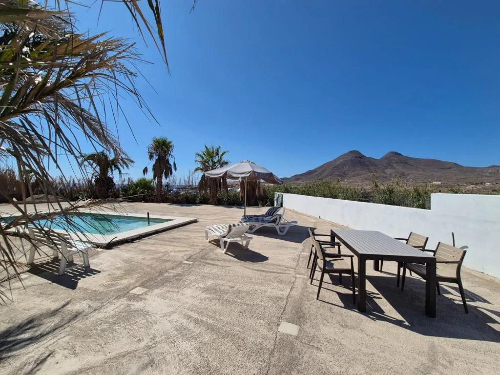 Terraza con piscina y mesa de comedor exterior entre palmeras y montañas