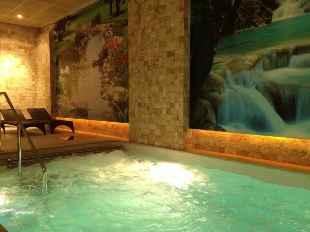 Piscina de spa con mural de cascada y tumbona junto al agua